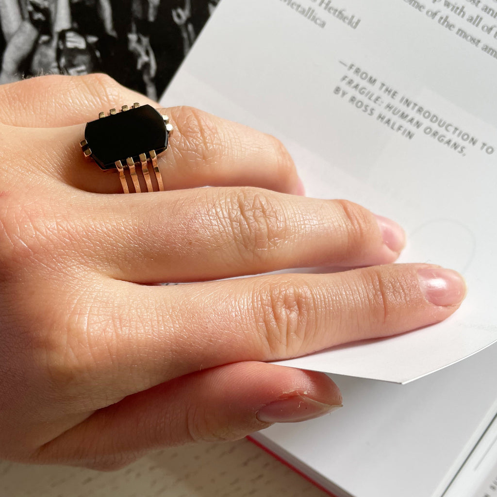 A woman's hand turning the page of a book and wearing a black onyx ring with four gold bands.