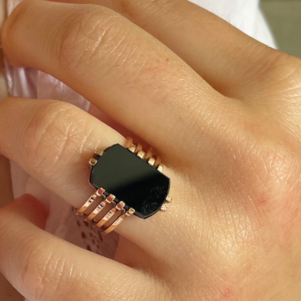 A close up picture of a woman wearing a black onyx ring set in gold.