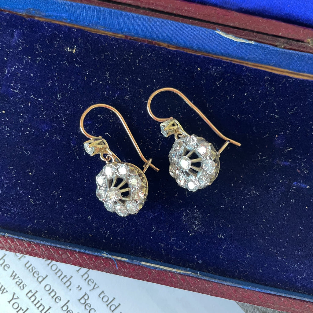Diamond cluster drop earrings in gold on blue velvet background.
