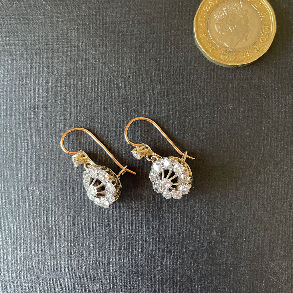Diamond cluster earrings on black background with a pound coin for size reference.