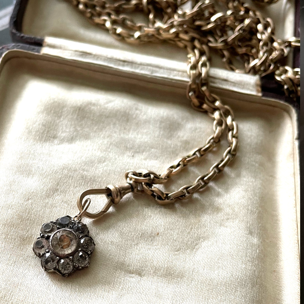 Flower-shaped diamond pendant on a gold chain in a ring box.