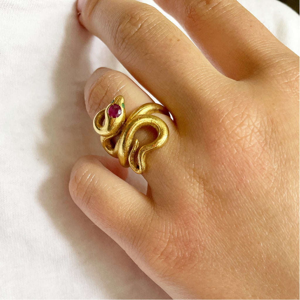 Gold snake ring on woman with emeralds and ruby.