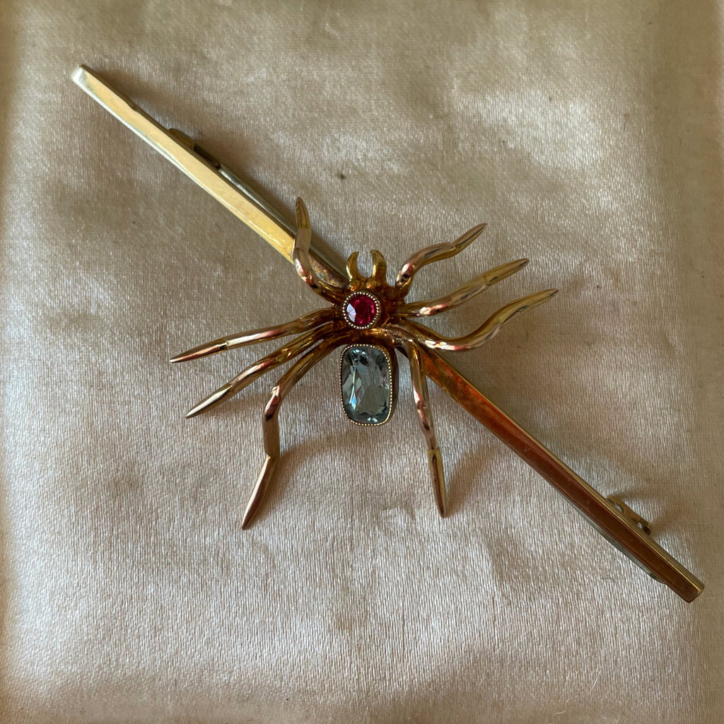 Gold spider brooch with ruby and aquamarine body.