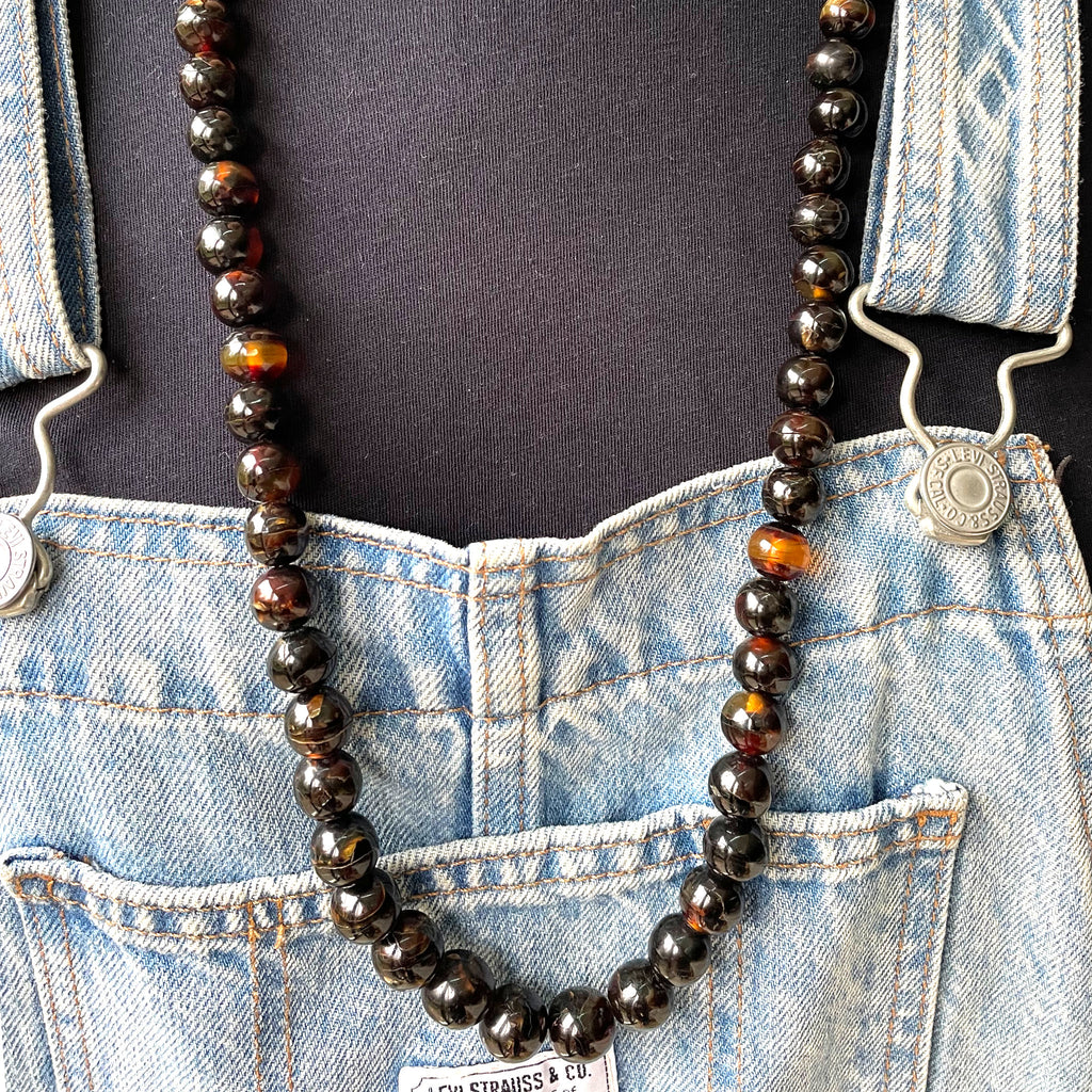Tortoiseshell necklace on woman wearing levis overalls and t shirt.