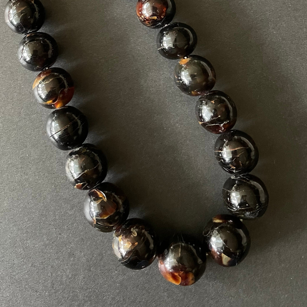 Detail of tortoiseshell beads on necklace on a black background.