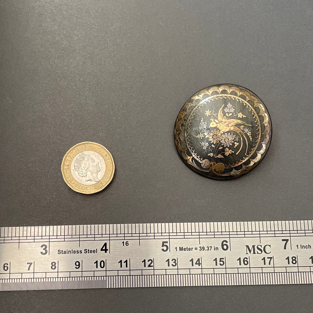 Tortoiseshell brooch with gold and silver next to metal ruler and pound coin for size.