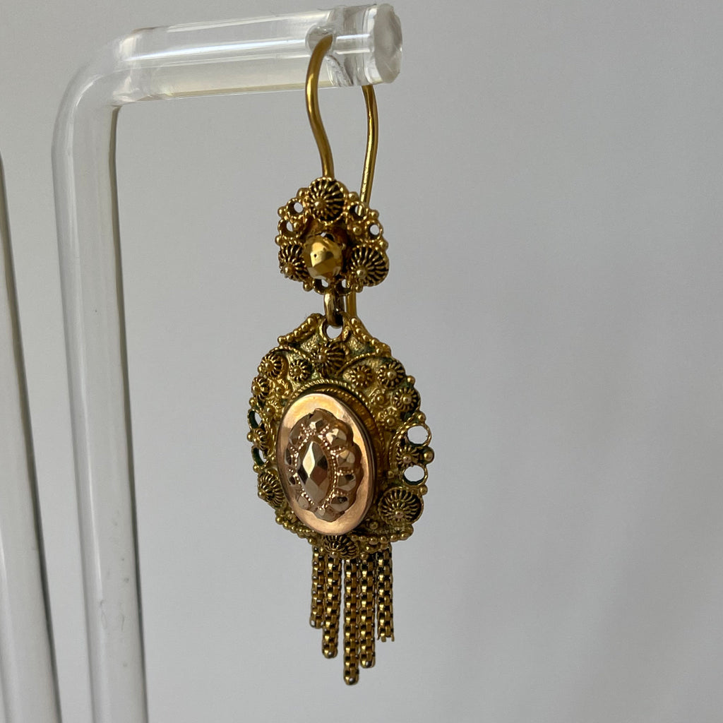 Gold earrings with tassels hanging on a display.