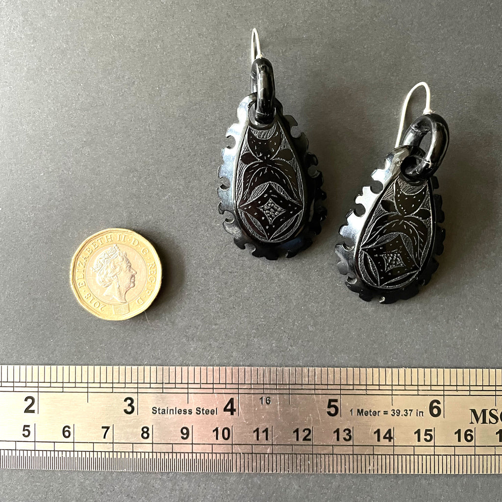 Whitby jet earrings next to a ruler and pound coin.