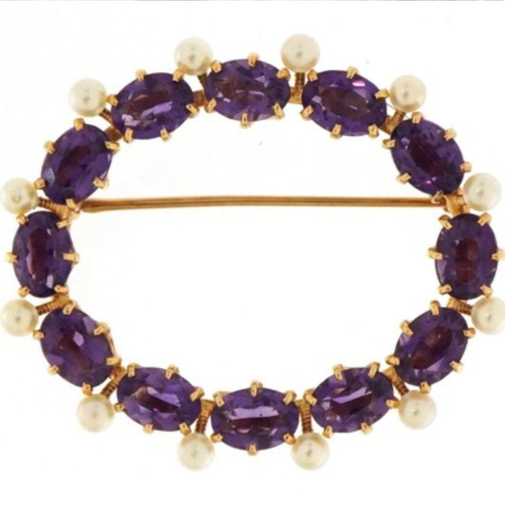 An oval brooch made of 14 carat yellow gold, twelve large amethysts, and 12 seed pearls.