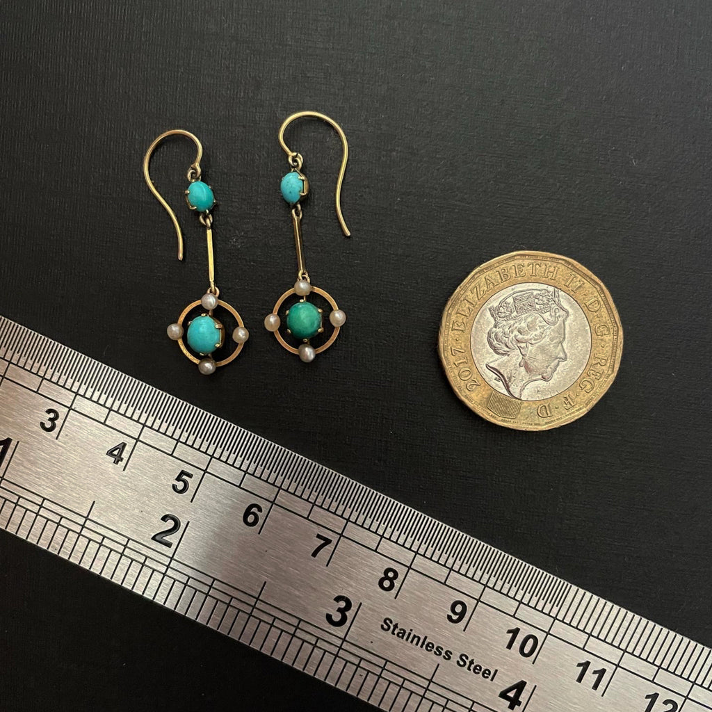 antique earrings of gold and pearls next to a metal ruler and pound coin
