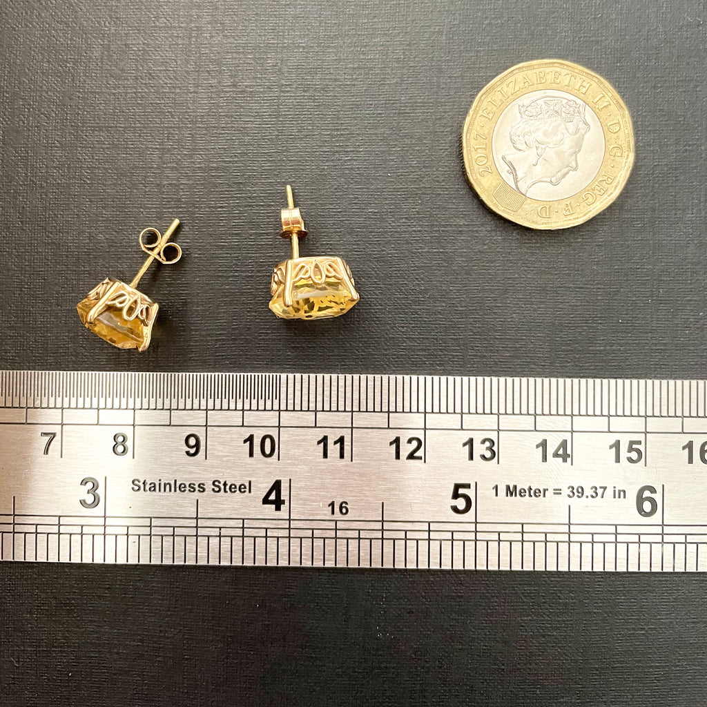 Large citrine stud earrings on black background next to a metal ruler.