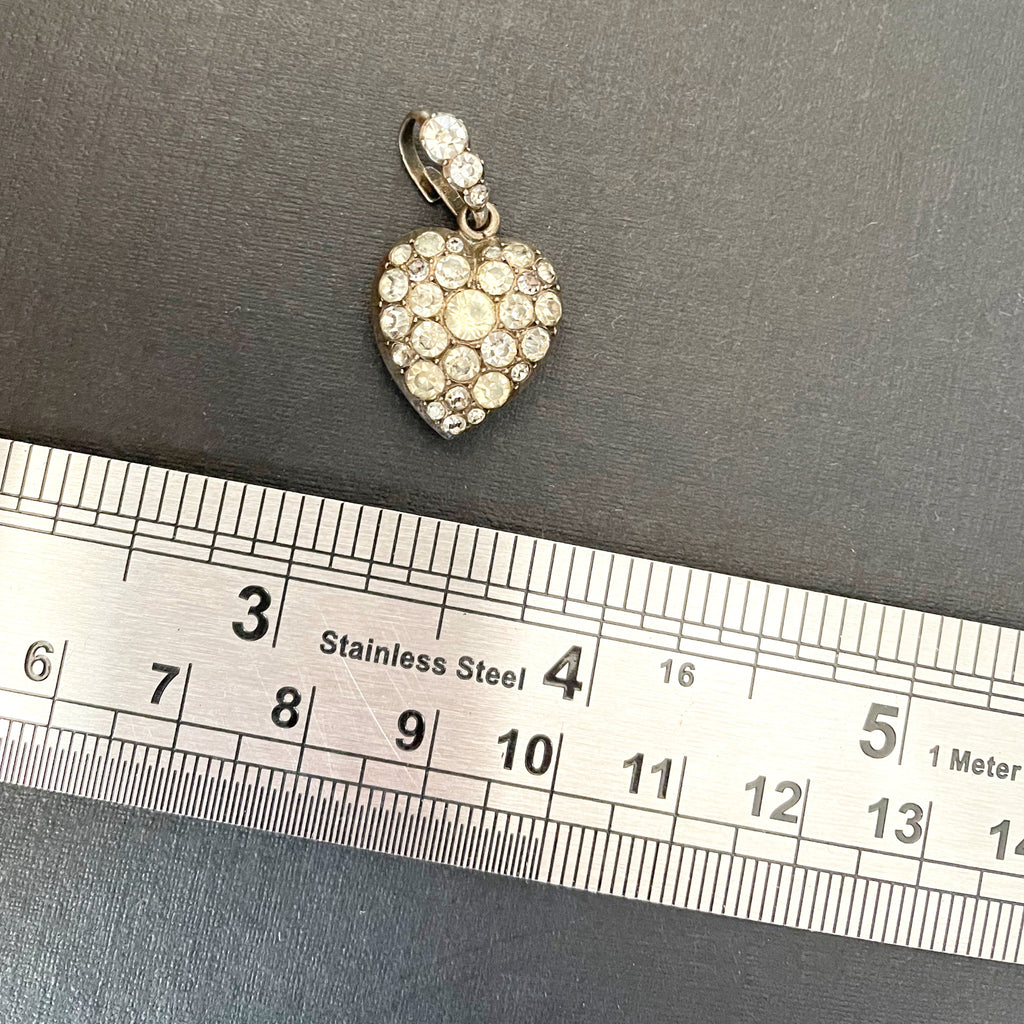 heart shaped pendant with colourless paste stones next to metal ruler